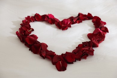 Photo of Heart made with rose petals on bed, closeup