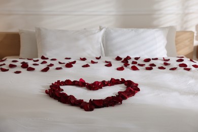 Photo of Heart made with rose petals on bed indoors
