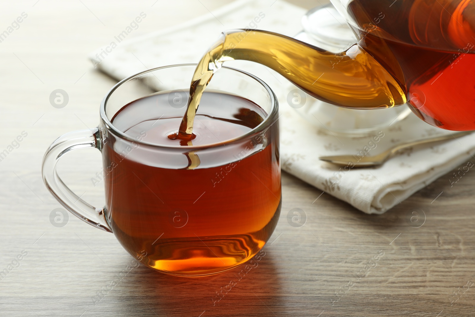 Pouring freshly brewed tea from teapot into cup at wooden table, closeup Photo of Pouring freshly brewed tea from teapot into cup at wooden table, closeup