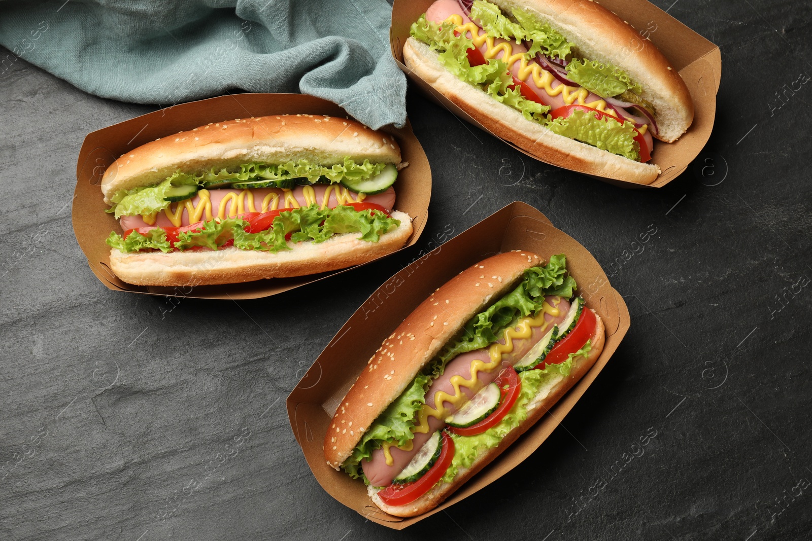 Tasty hot dogs with vegetables on black table, flat lay Photo of Tasty hot dogs with vegetables on black table, flat lay