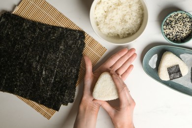 Photo of Woman making tasty onigiri (Japanese rice balls) at white table, top view