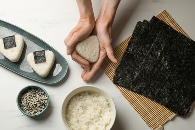 Photo of Woman making tasty onigiri (Japanese rice balls) at white table, top view
