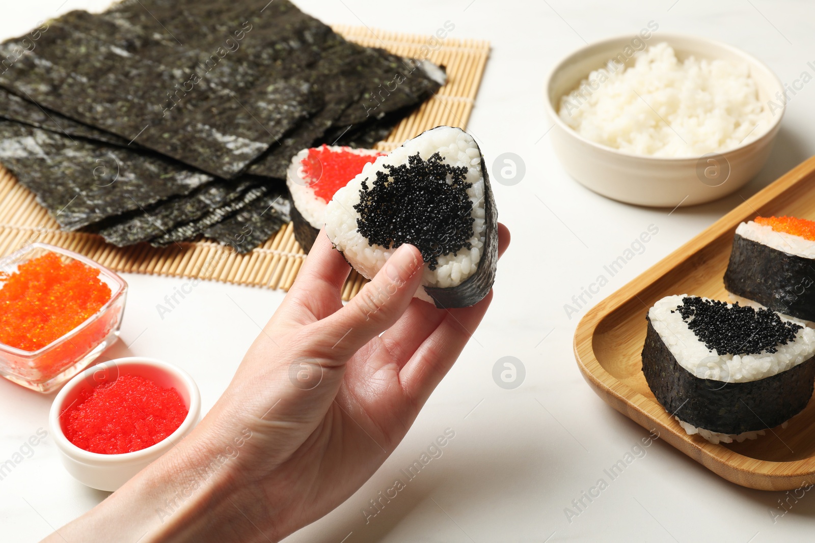 Woman with tasty tobiko onigiri (Japanese rice balls) at white marble table, closeup Photo of Woman with tasty tobiko onigiri (Japanese rice balls) at white marble table, closeup
