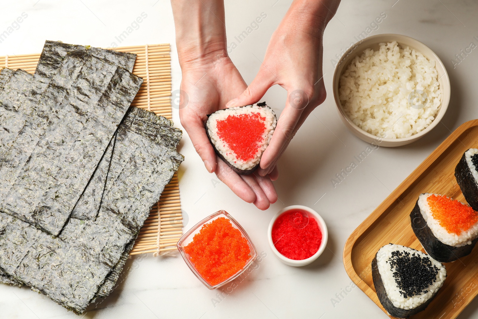 Woman with tasty tobiko onigiri (Japanese rice balls) at white marble table, top view Photo of Woman with tasty tobiko onigiri (Japanese rice balls) at white marble table, top view