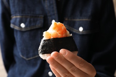 Photo of Woman with tasty onigiri (Japanese rice ball) indoors, closeup