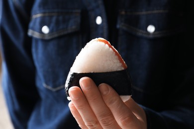 Photo of Woman with tasty onigiri (Japanese rice ball) indoors, closeup