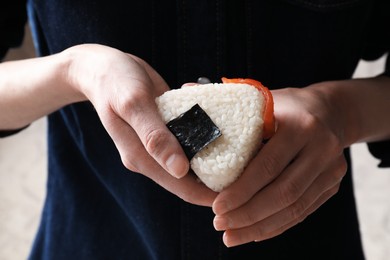 Photo of Woman with tasty onigiri (Japanese rice ball) indoors, closeup