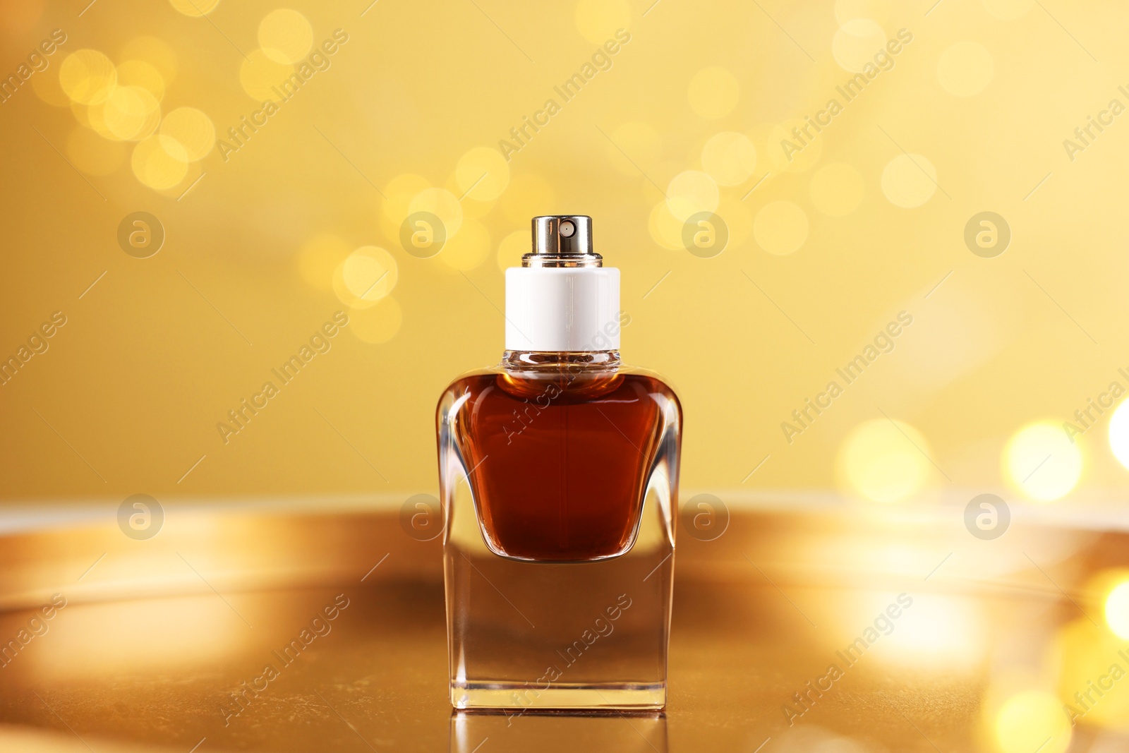 Bottle of aromatic perfume on metal tray against beige background with blurred lights, closeup. Bokeh effect Photo of Bottle of aromatic perfume on metal tray against beige background with blurred lights, closeup. Bokeh effect