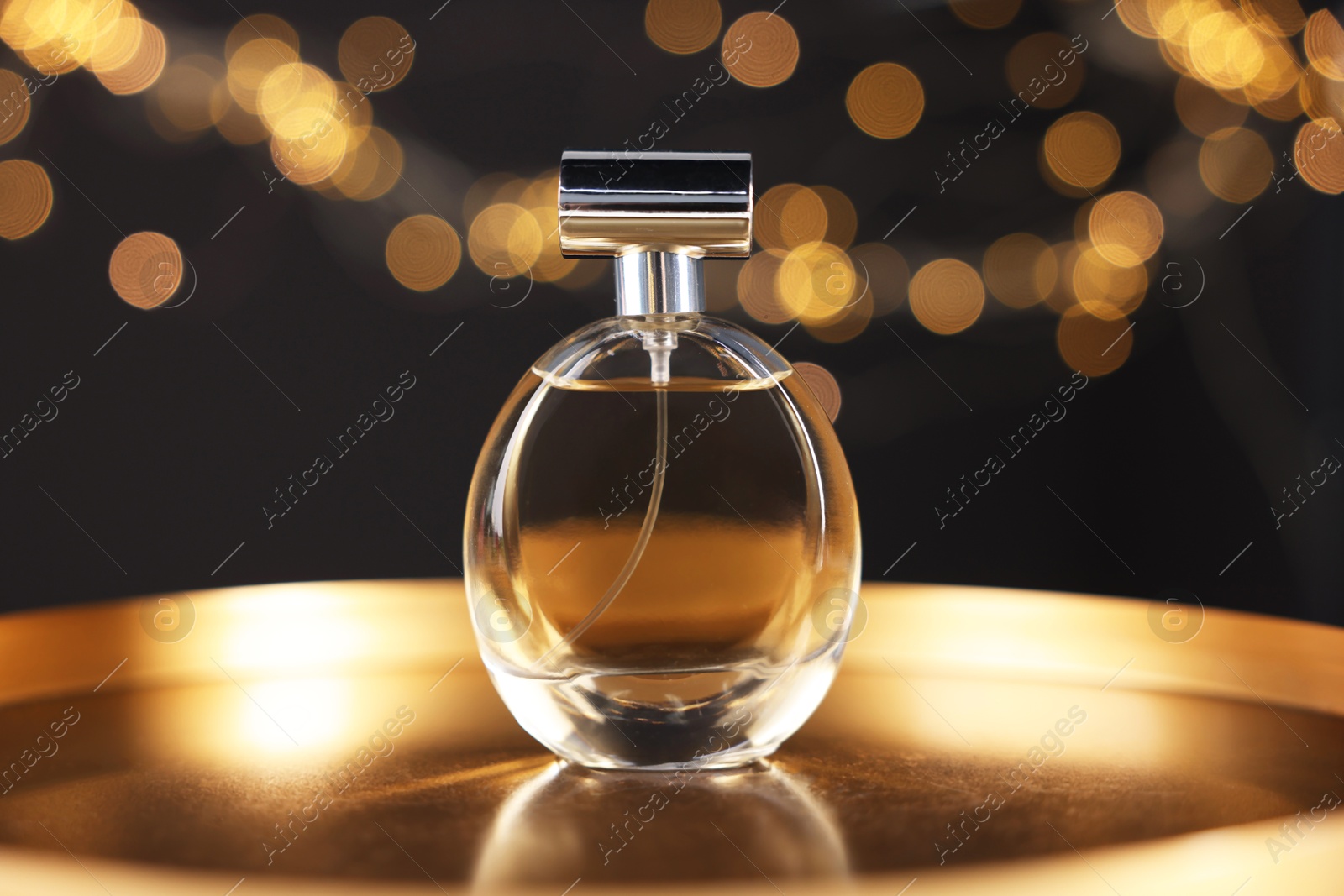Bottle of aromatic perfume on metal tray against black background with blurred lights, closeup. Bokeh effect Photo of Bottle of aromatic perfume on metal tray against black background with blurred lights, closeup. Bokeh effect