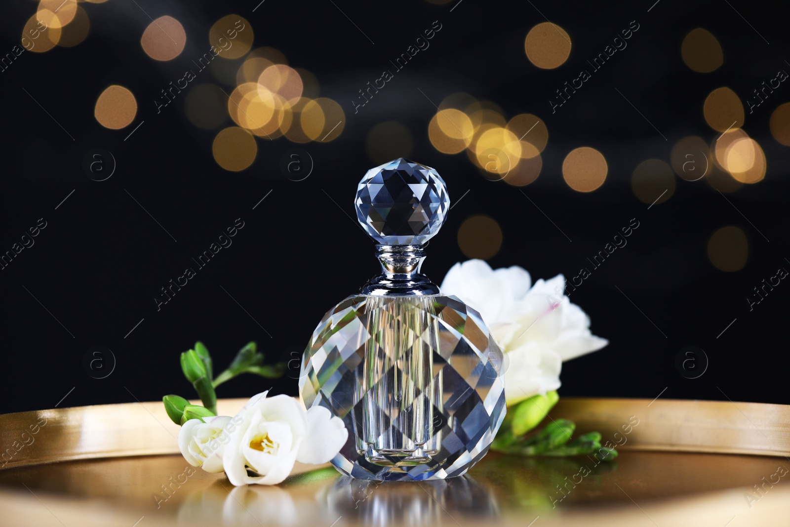 Bottle of aromatic perfume and flowers on metal tray against black background with blurred lights, closeup. Bokeh effect Photo of Bottle of aromatic perfume and flowers on metal tray against black background with blurred lights, closeup. Bokeh effect