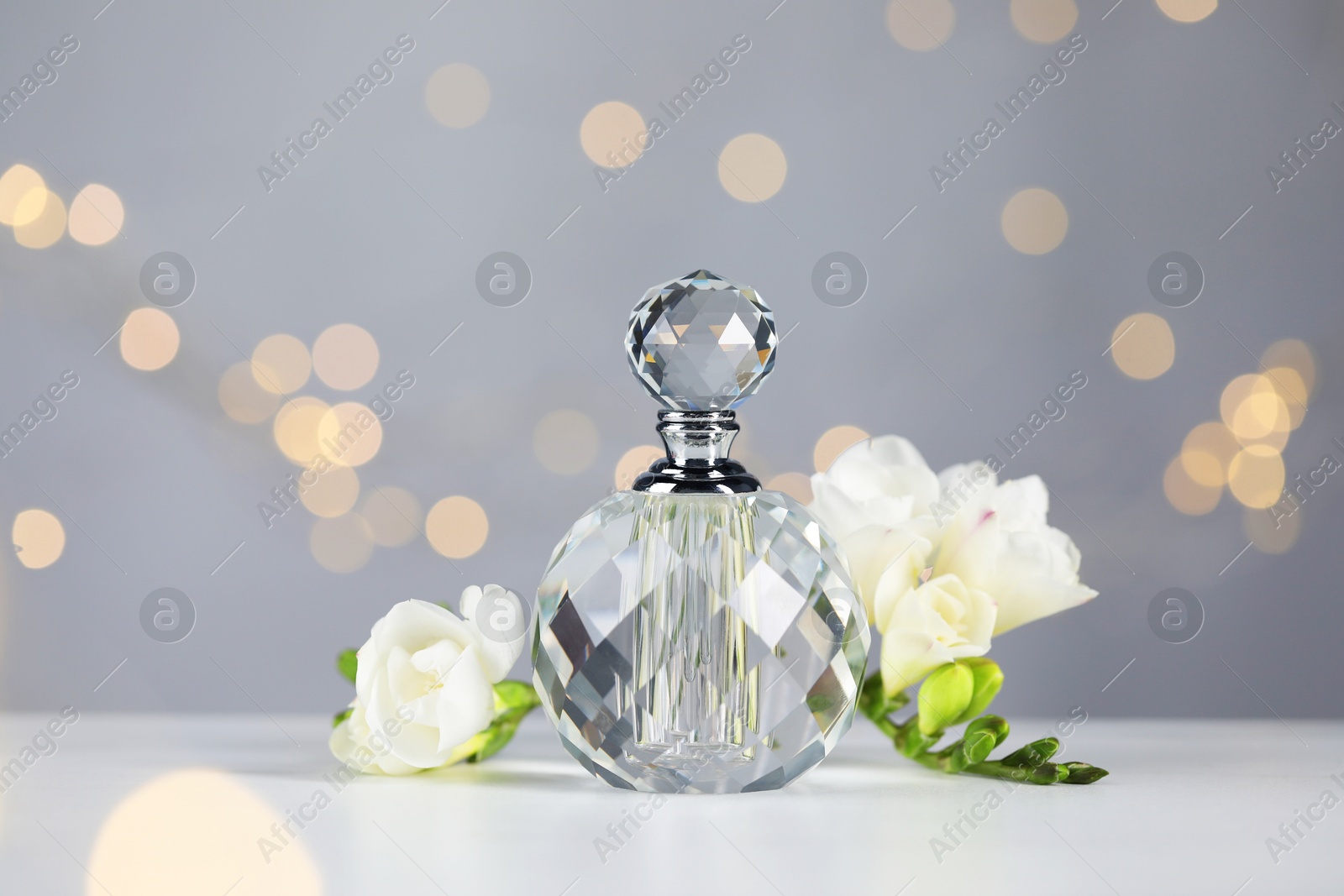 Bottle of aromatic perfume and flowers on light table against grey background with blurred lights, closeup. Bokeh effect Photo of Bottle of aromatic perfume and flowers on light table against grey background with blurred lights, closeup. Bokeh effect