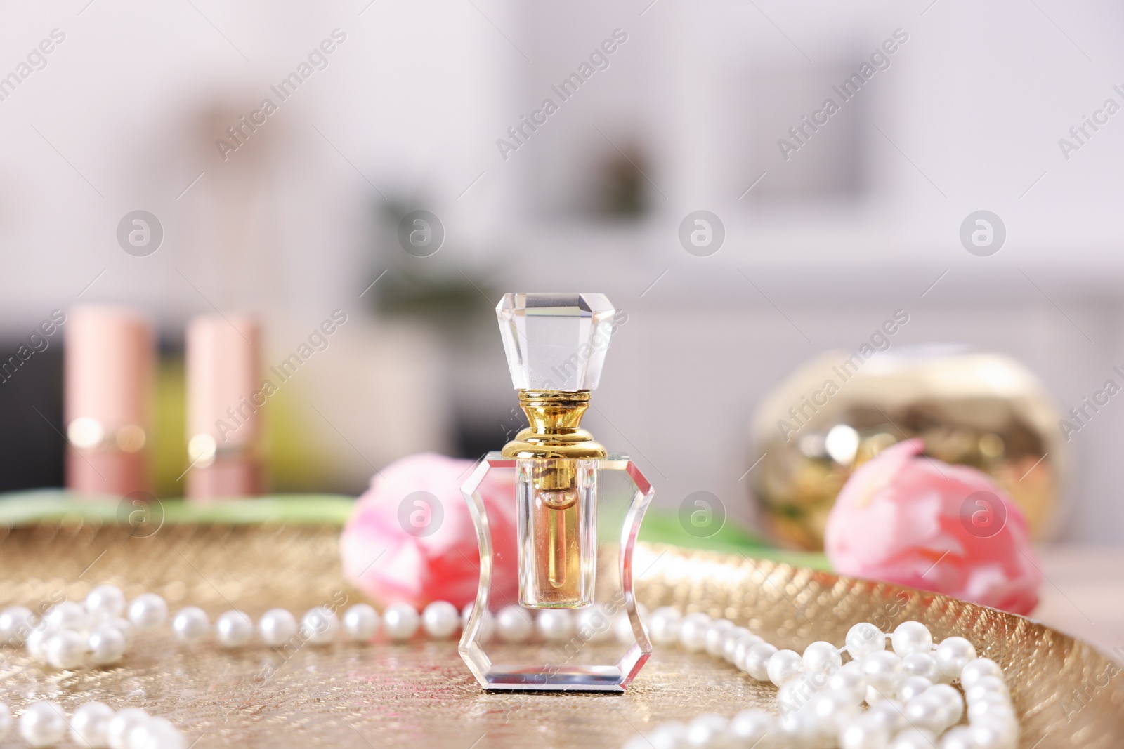 Bottle of aromatic perfume, necklace and flowers on textured plate against blurred background, closeup Photo of Bottle of aromatic perfume, necklace and flowers on textured plate against blurred background, closeup