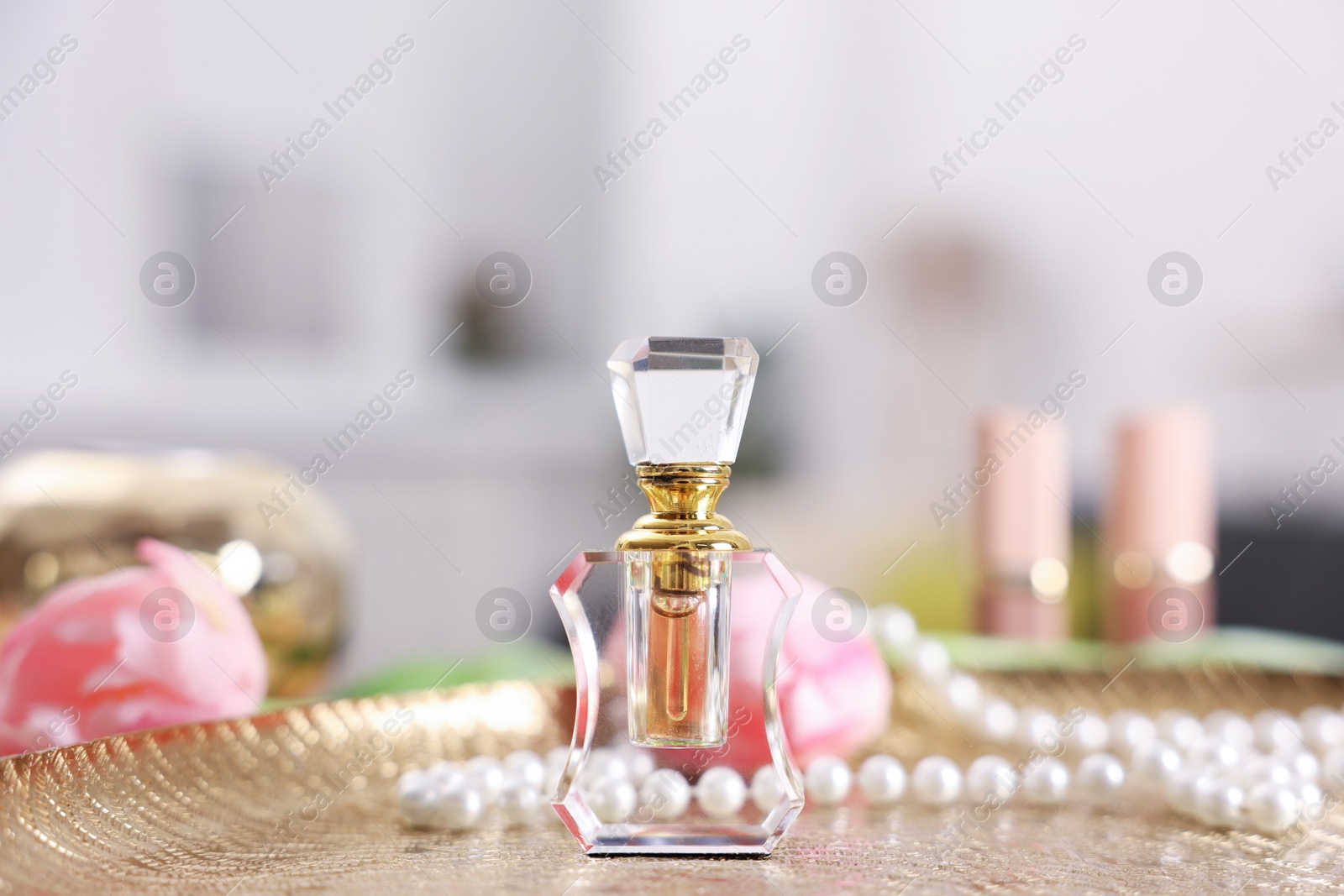 Bottle of aromatic perfume, necklace and flowers on textured plate against blurred background, closeup Photo of Bottle of aromatic perfume, necklace and flowers on textured plate against blurred background, closeup
