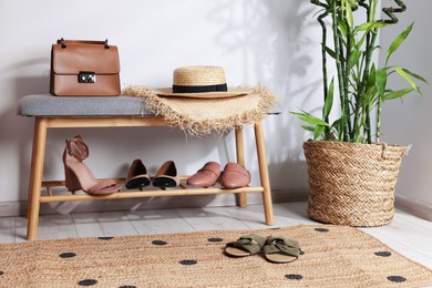 Photo of Stand with different stylish shoes, straw hats, bag and houseplant indoors