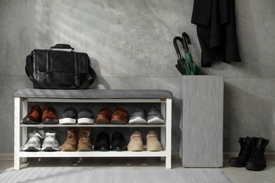 Photo of Shoe storage bench with different footwear, briefcase and umbrellas indoors