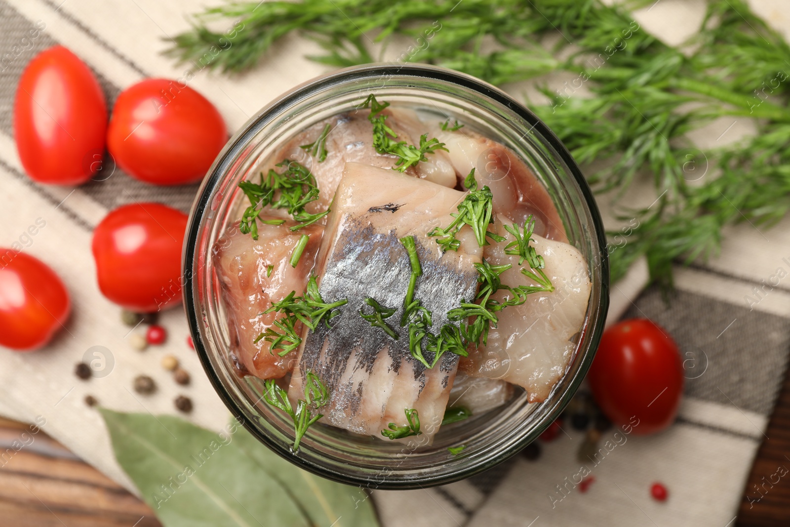 Pieces of delicious herring with dill in jar and tomatoes on table, flat lay Photo of Pieces of delicious herring with dill in jar and tomatoes on table, flat lay