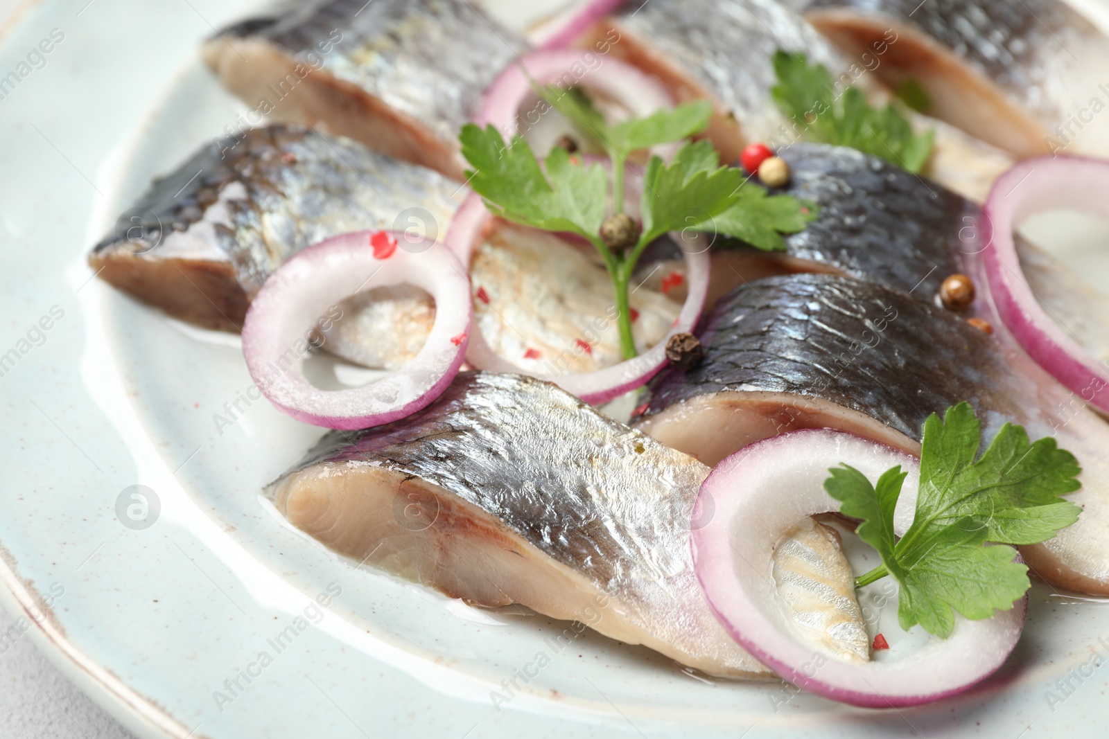 Photo of Pieces of delicious herring with spices and onions on plate, closeup