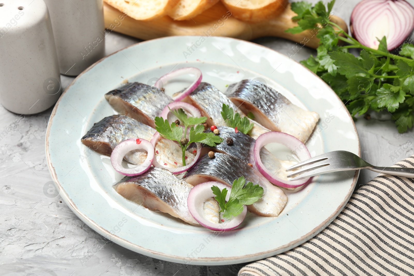 Pieces of delicious herring with spices and onions served on grey textured table, closeup Photo of Pieces of delicious herring with spices and onions served on grey textured table, closeup