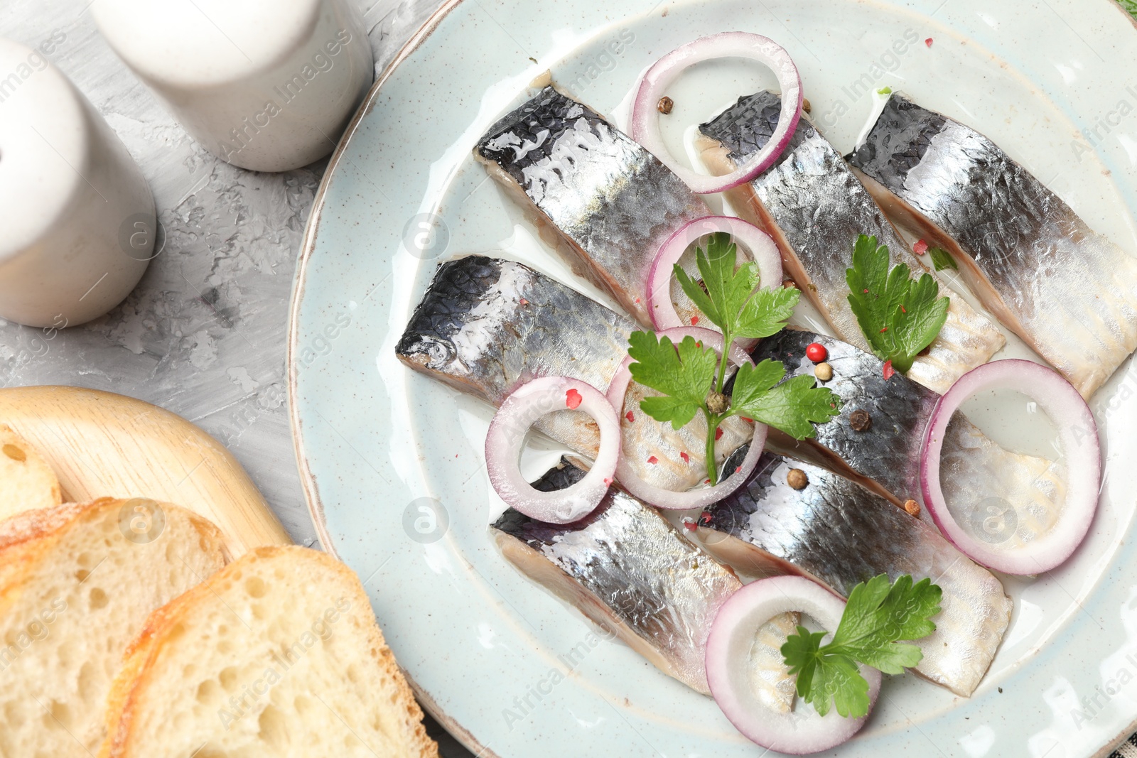 Pieces of delicious herring with spices and onions served on grey textured table, flat lay Photo of Pieces of delicious herring with spices and onions served on grey textured table, flat lay