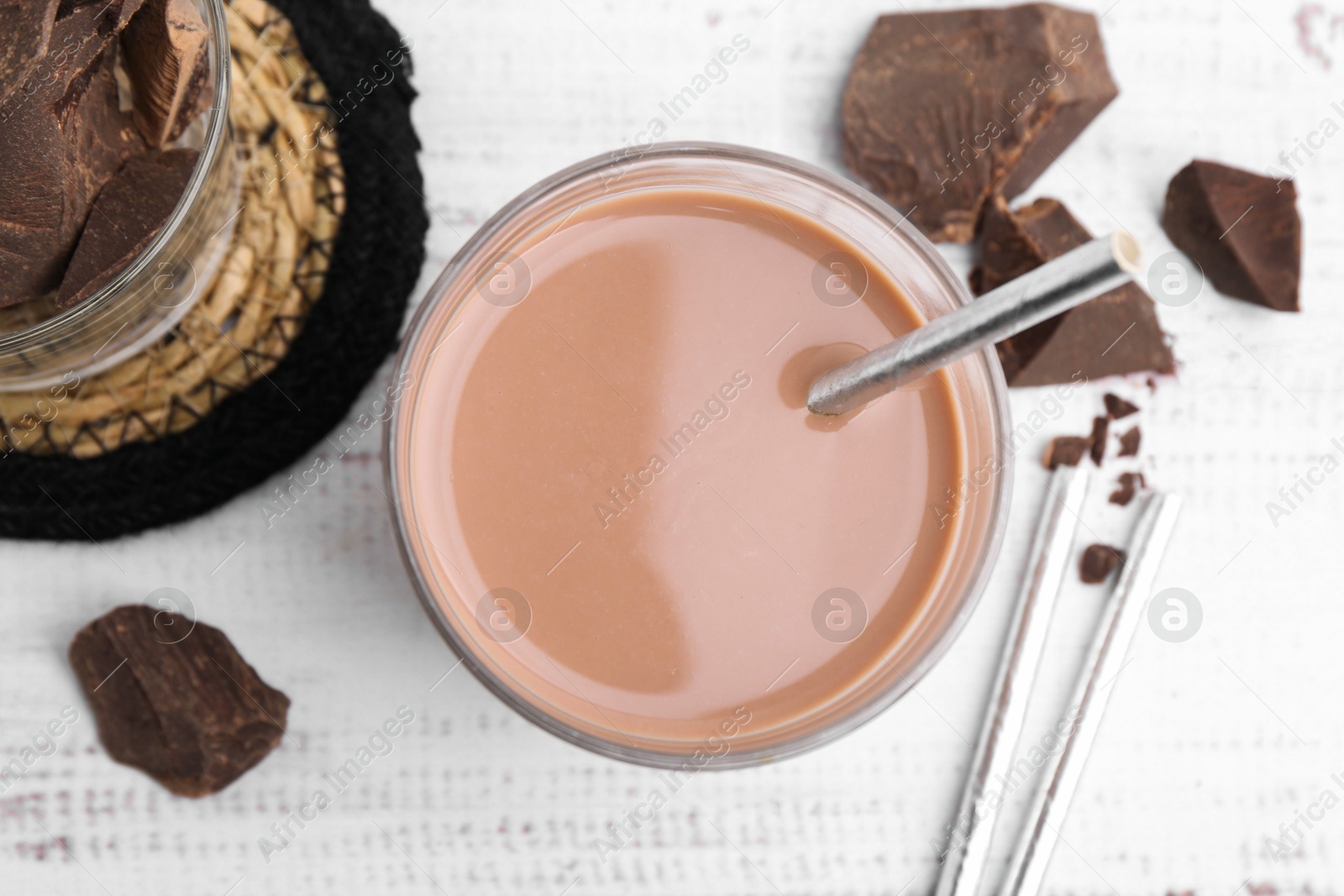 Tasty chocolate milk in glass and pieces of chocolate on white wooden table, flat lay Photo of Tasty chocolate milk in glass and pieces of chocolate on white wooden table, flat lay