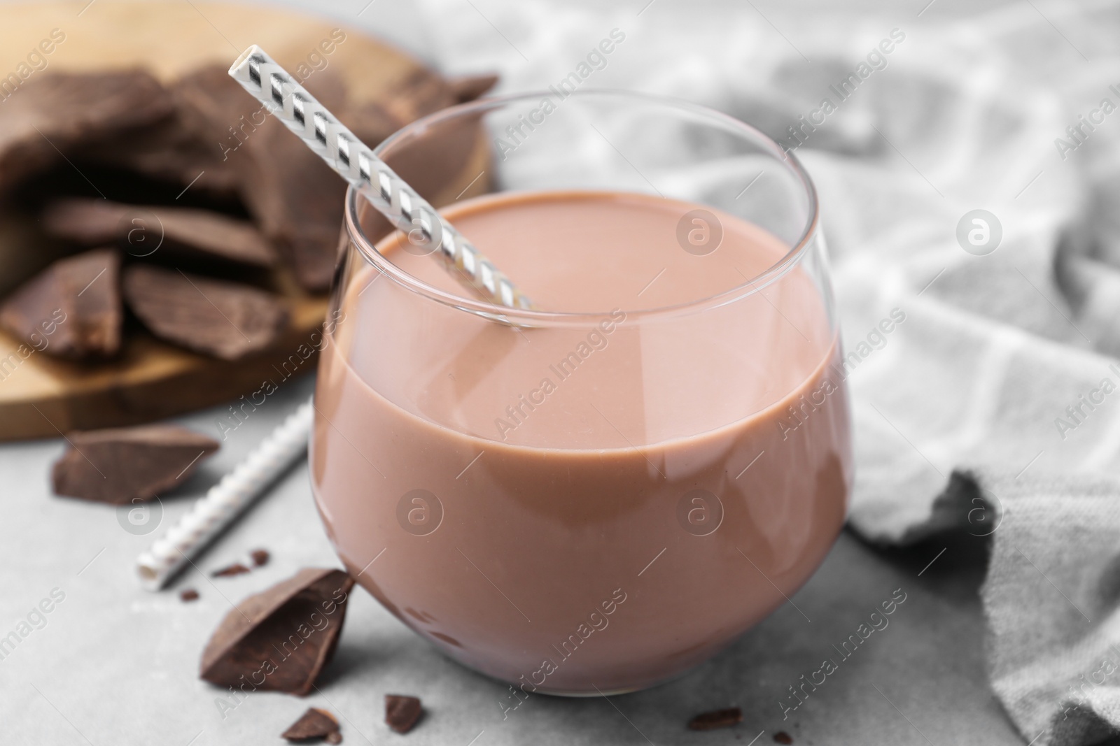 Tasty chocolate milk in glass and pieces of chocolate on light grey table, closeup Photo of Tasty chocolate milk in glass and pieces of chocolate on light grey table, closeup