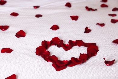 Photo of Heart made with beautiful rose petals on bed