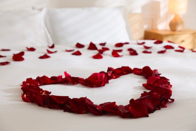 Photo of Heart made with rose petals on bed indoors, closeup