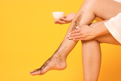 Photo of Woman applying body scrub onto her leg on orange background, closeup. Space for text
