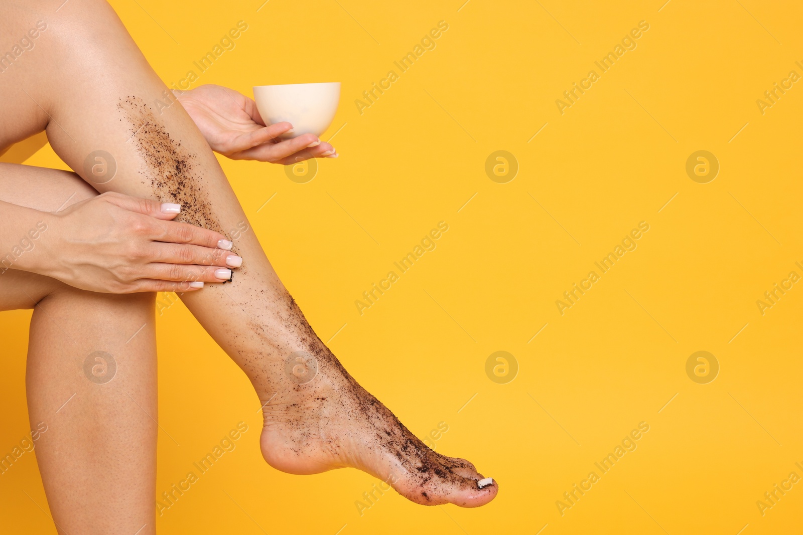 Woman applying body scrub onto her leg on orange background, closeup. Space for text Photo of Woman applying body scrub onto her leg on orange background, closeup. Space for text