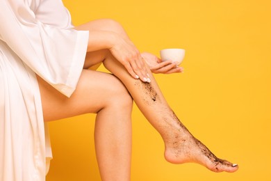 Photo of Woman applying body scrub onto her leg on orange background, closeup