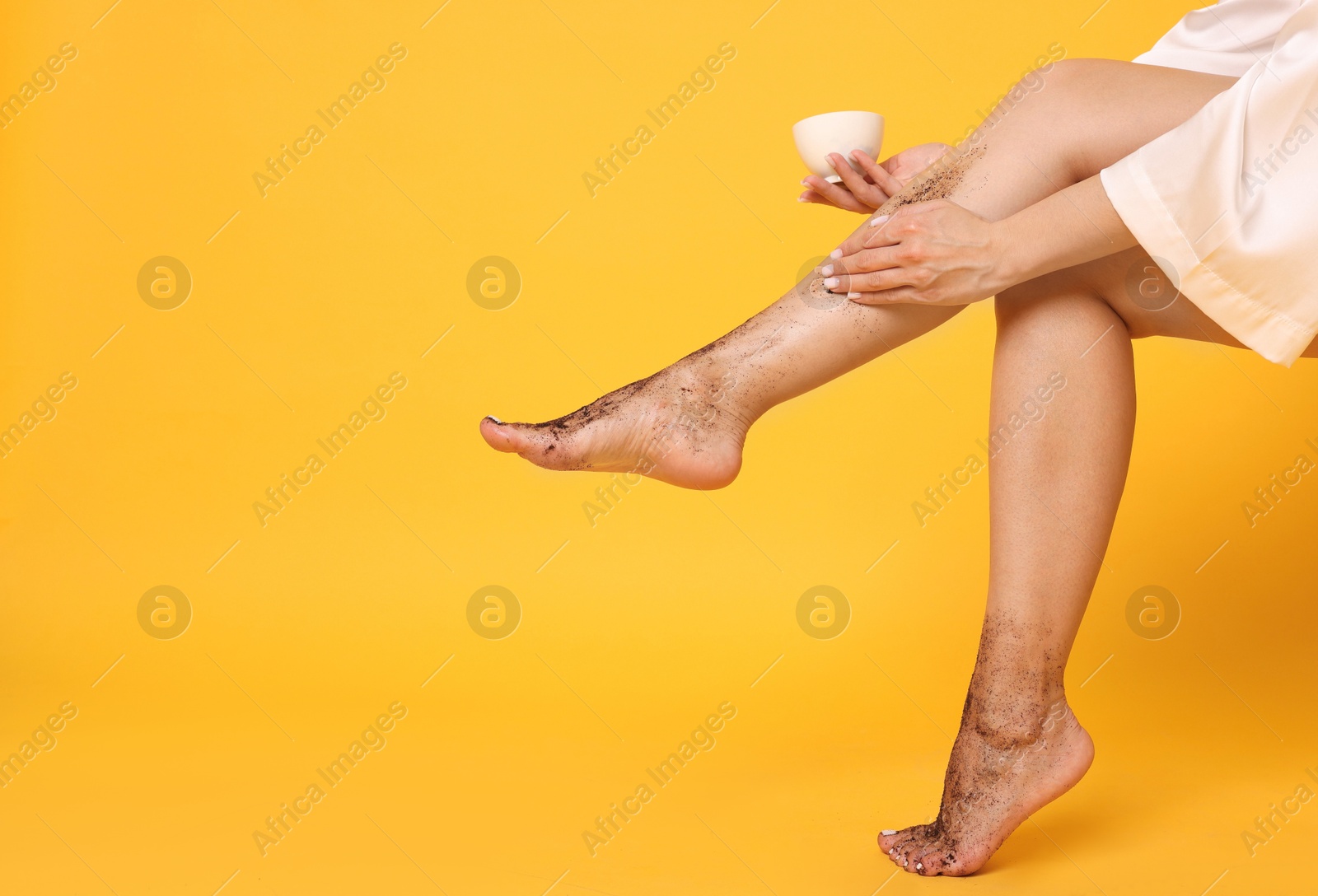 Woman applying body scrub onto her leg on orange background, closeup. Space for text Photo of Woman applying body scrub onto her leg on orange background, closeup. Space for text