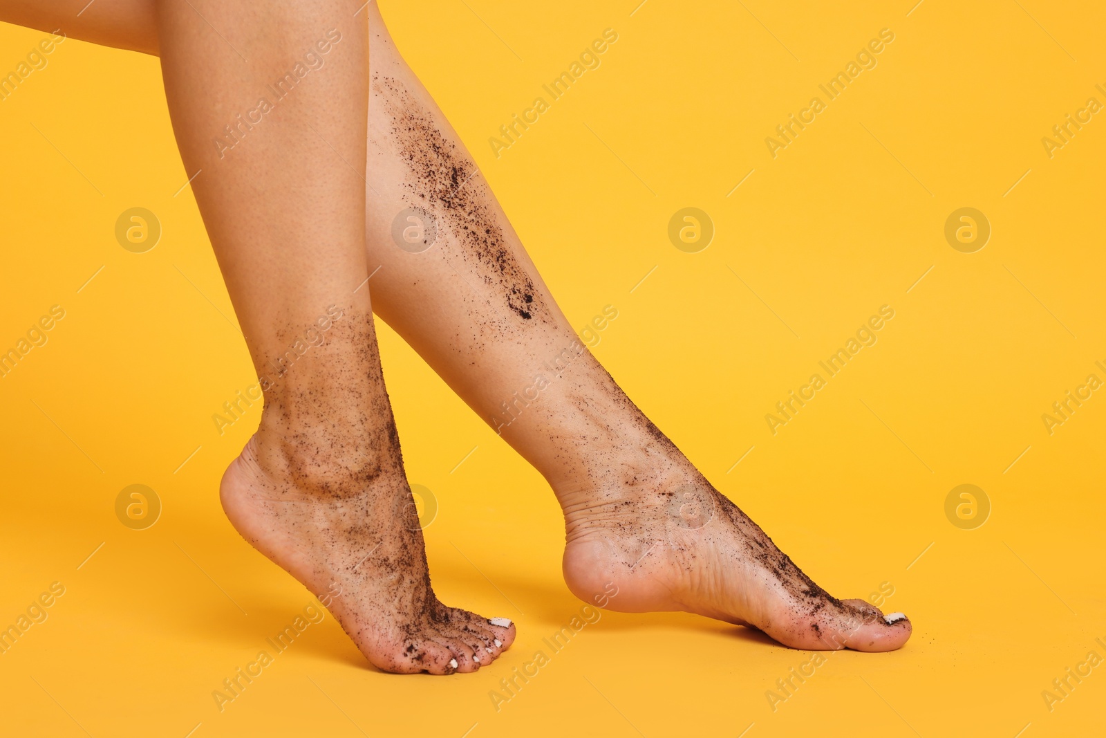 Woman with body scrub on her legs against orange background, closeup Photo of Woman with body scrub on her legs against orange background, closeup