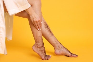 Photo of Woman applying body scrub onto her leg on orange background, closeup