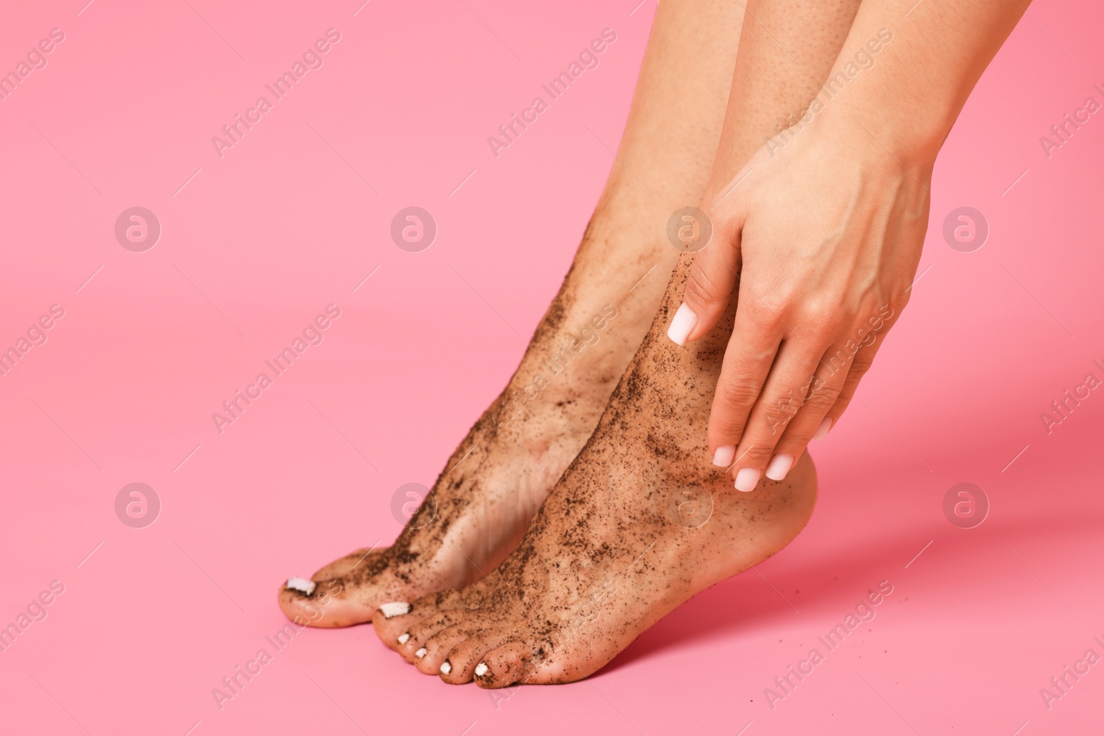 Woman applying body scrub onto her feet on pink background, closeup Photo of Woman applying body scrub onto her feet on pink background, closeup