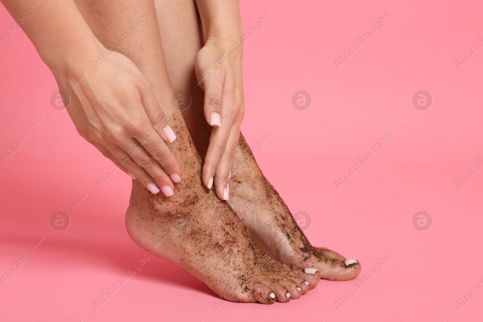 Woman applying body scrub onto her feet on pink background, closeup Photo of Woman applying body scrub onto her feet on pink background, closeup