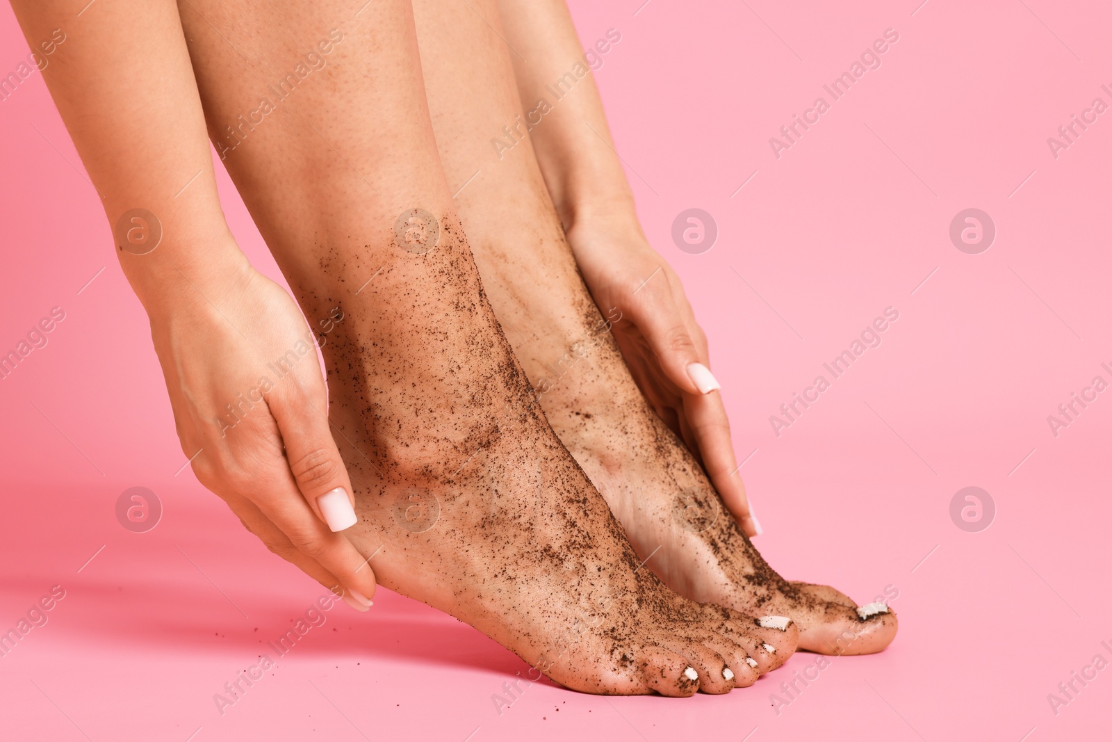 Woman applying body scrub onto her feet on pink background, closeup Photo of Woman applying body scrub onto her feet on pink background, closeup
