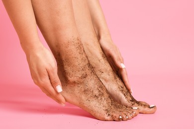 Photo of Woman applying body scrub onto her feet on pink background, closeup