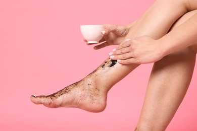 Photo of Woman applying body scrub onto her leg on pink background, closeup