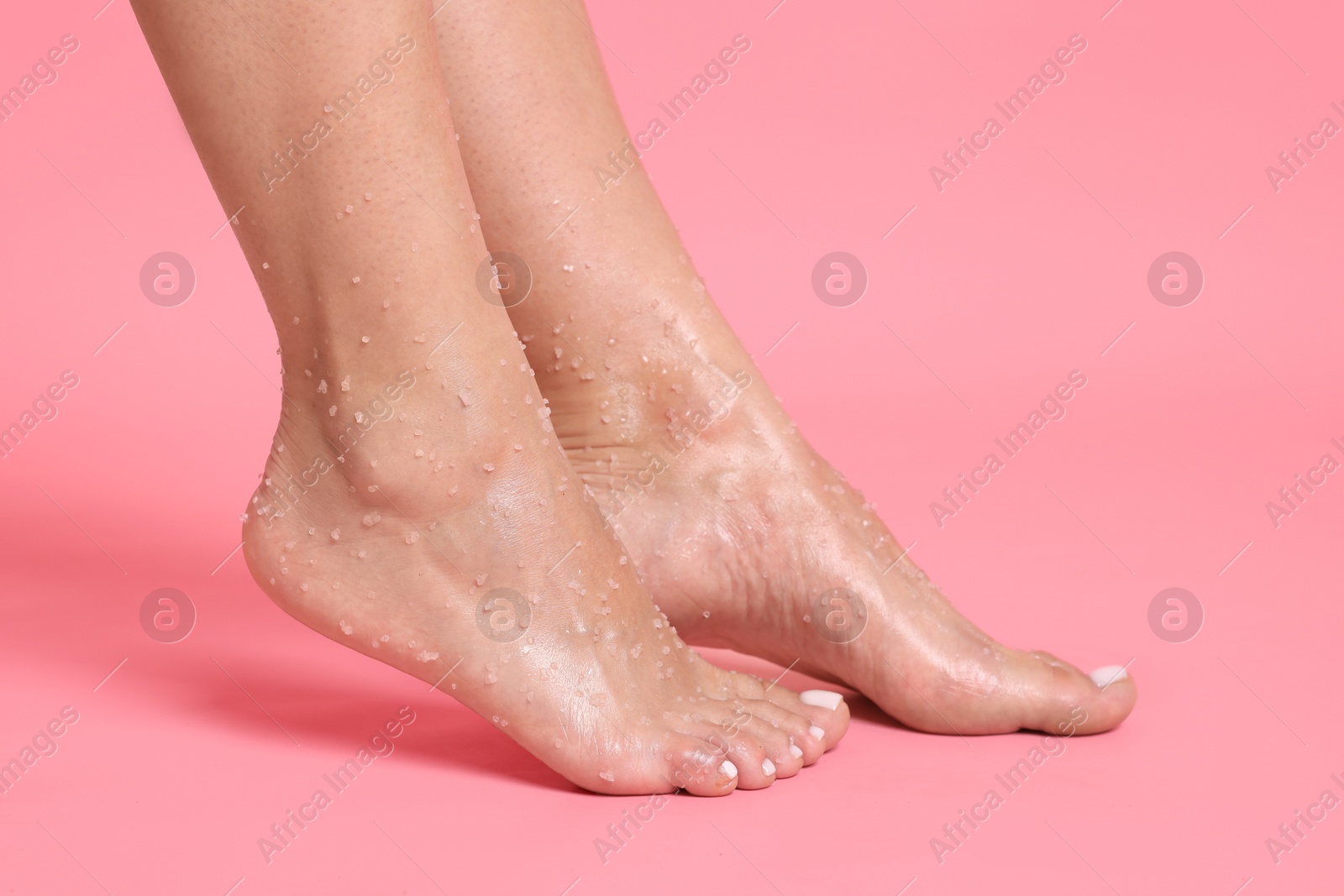 Woman with body scrub on her feet against pink background, closeup Photo of Woman with body scrub on her feet against pink background, closeup