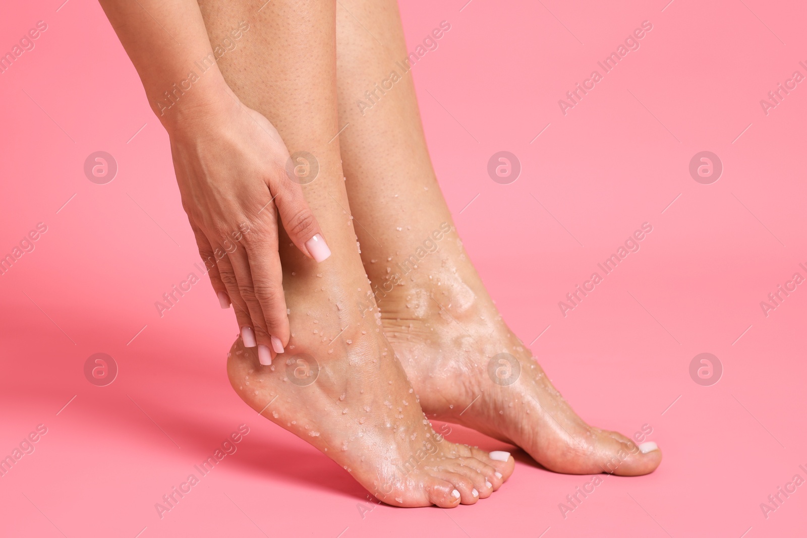 Woman applying body scrub onto her feet on pink background, closeup Photo of Woman applying body scrub onto her feet on pink background, closeup