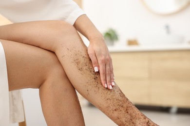 Photo of Woman applying body scrub onto her leg indoors, closeup