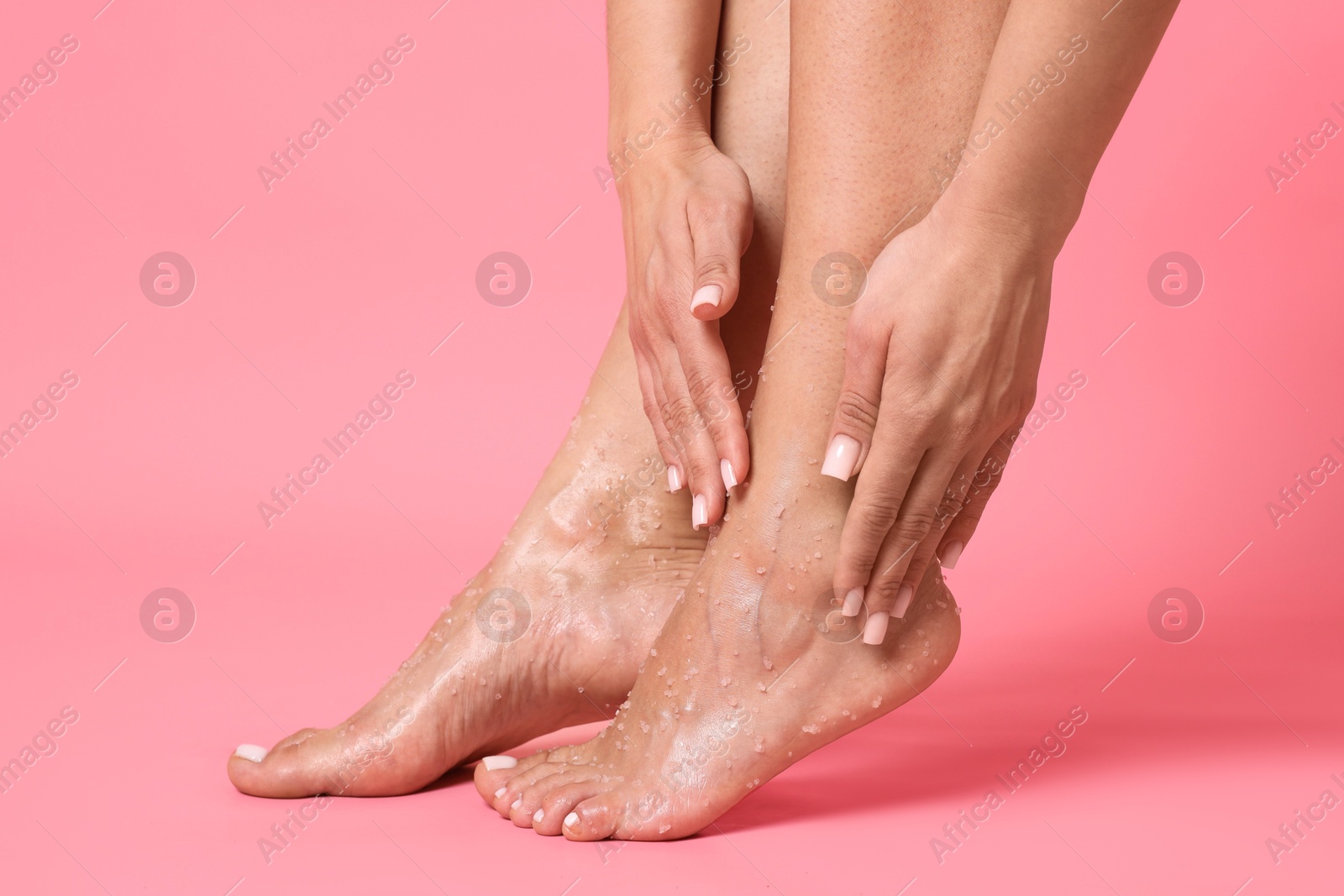 Woman applying body scrub onto her feet on pink background, closeup Photo of Woman applying body scrub onto her feet on pink background, closeup