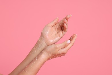 Photo of Woman applying body scrub onto her hands on pink background, closeup