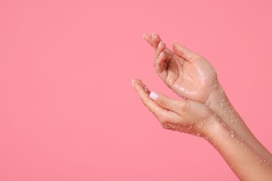 Photo of Woman applying body scrub onto her hands on pink background, closeup. Space for text