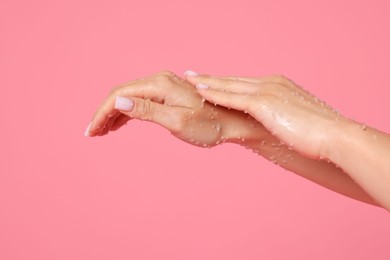 Photo of Woman applying body scrub onto her hands on pink background, closeup