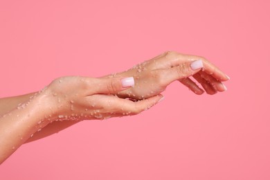 Photo of Woman applying body scrub onto her hands on pink background, closeup