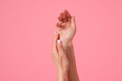 Photo of Woman applying body scrub onto her hands on pink background, closeup