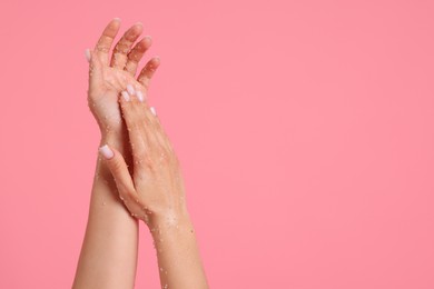 Photo of Woman applying body scrub onto her hands on pink background, closeup. Space for text