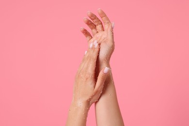 Photo of Woman applying body scrub onto her hands on pink background, closeup