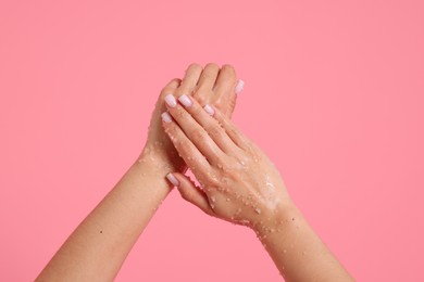 Photo of Woman applying body scrub onto her hands on pink background, closeup
